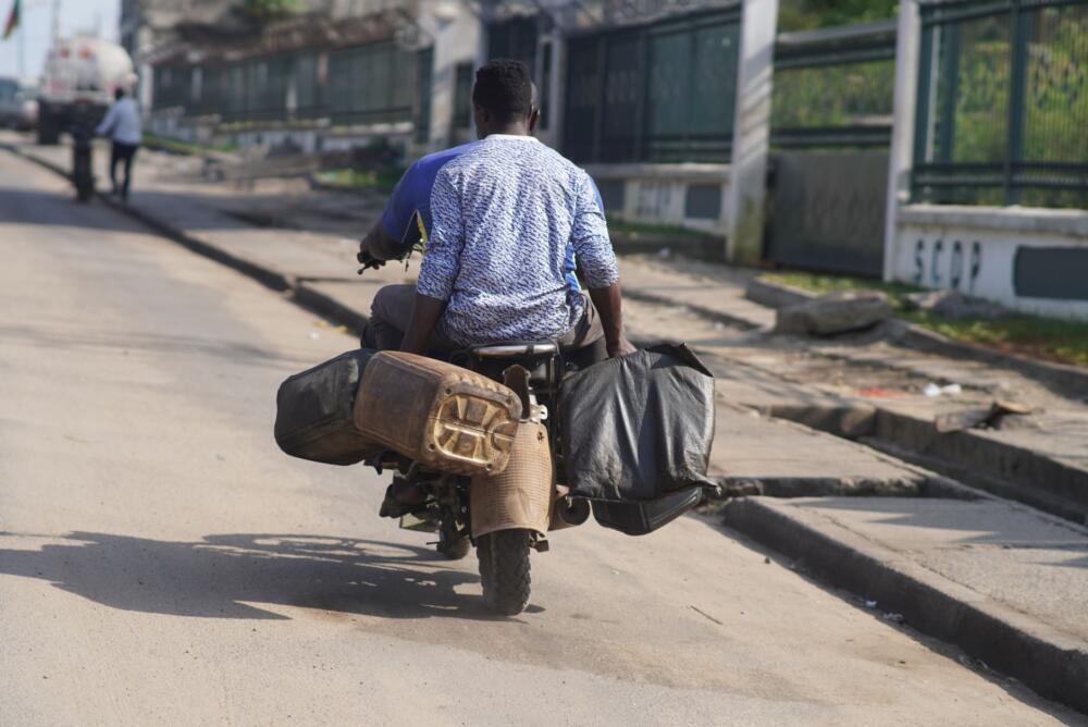 A man rides a motorbike with luggage on a sunny day in Douala, Cameroon.